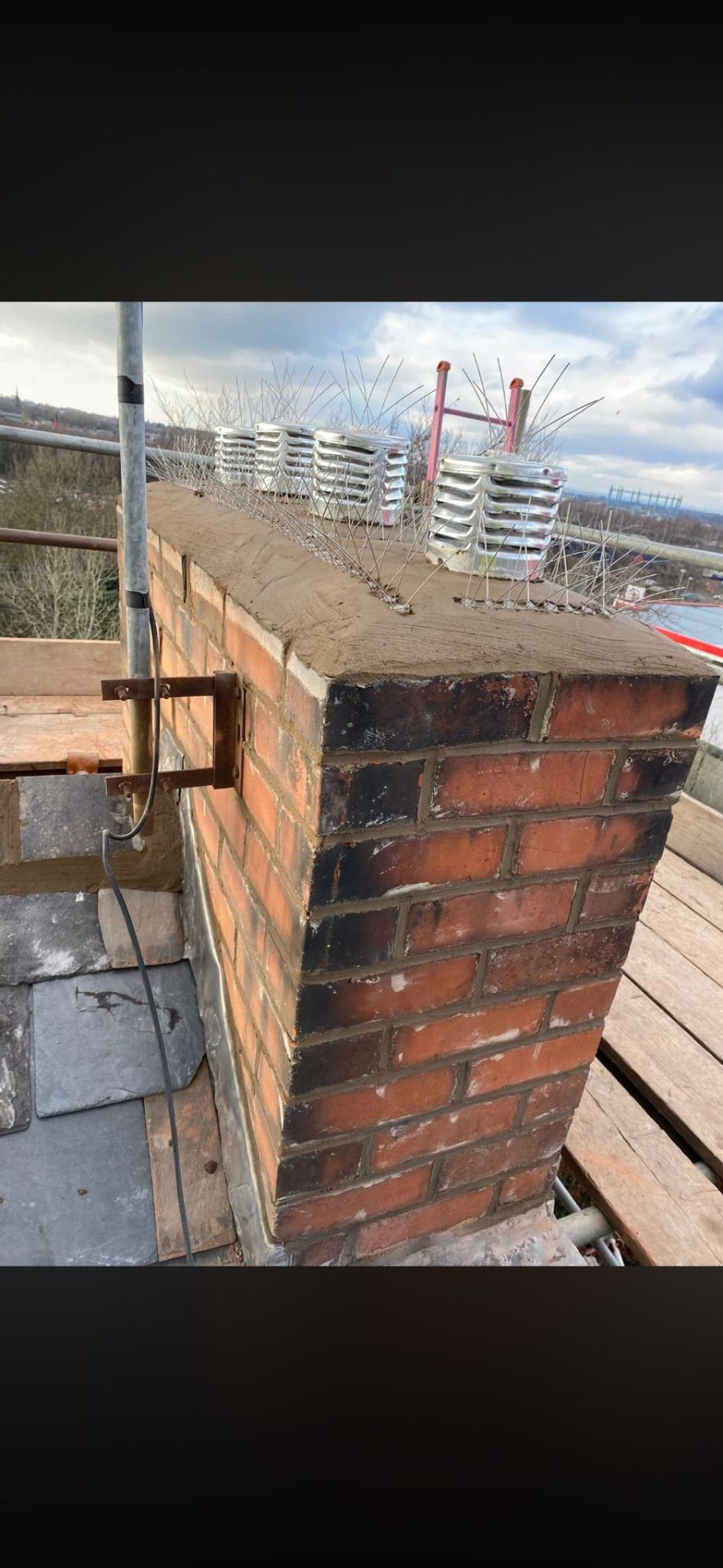 Repaired brick chimney with new pots and bird spikes beside slate roof