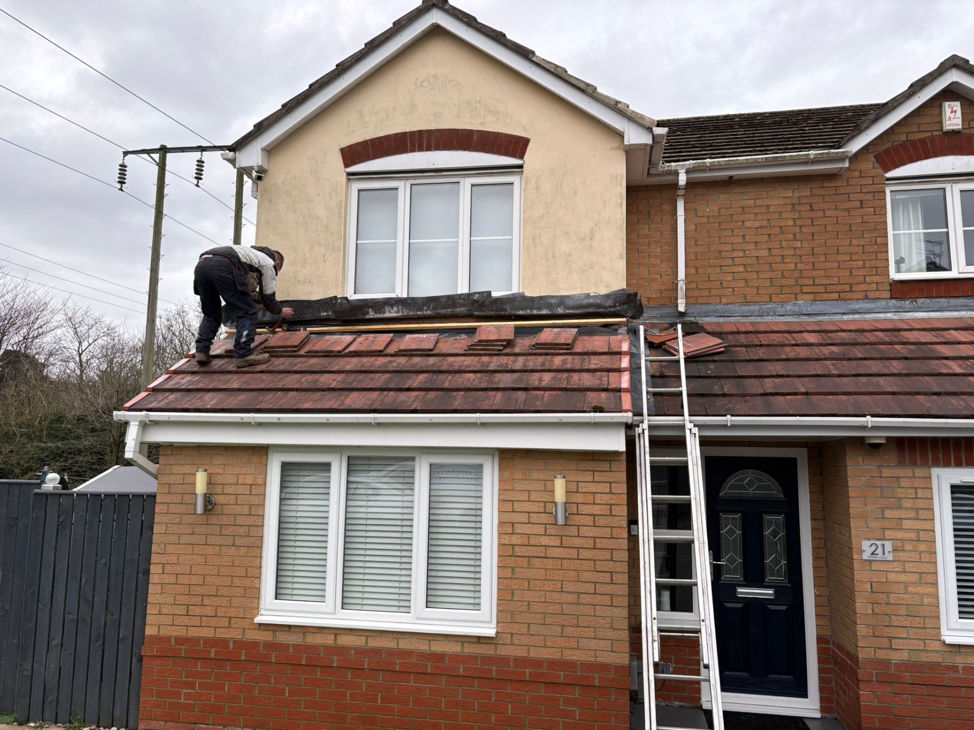 Roofer carrying out repairs on a pitched tiled roof above a flat-roof extension