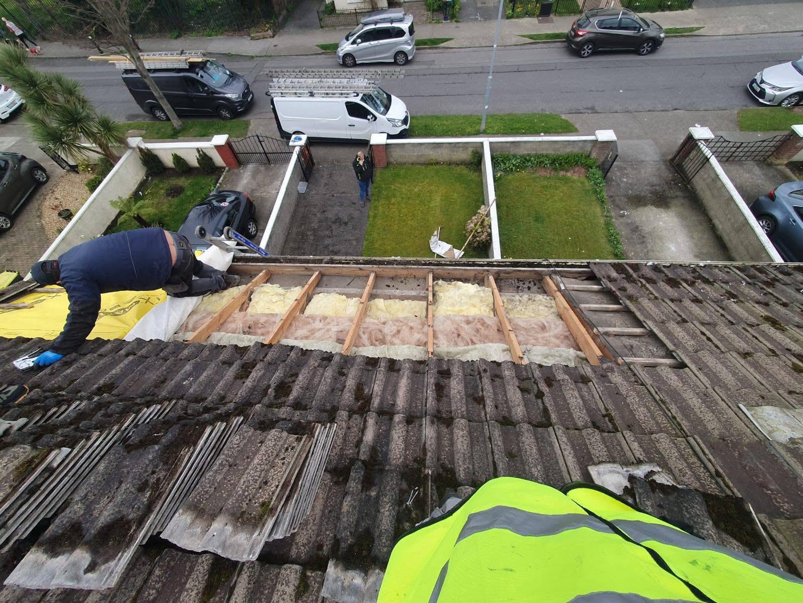 Roofer working on a pitched roof with exposed insulation and broken tiles