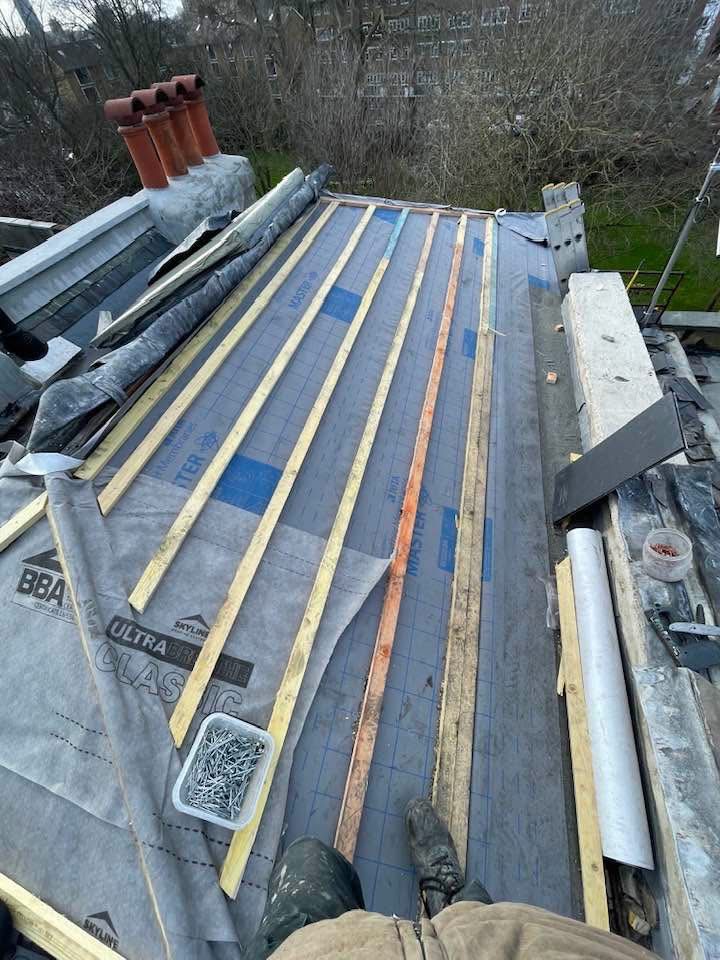 New roofing underlayment and timber battens being installed beside a chimney