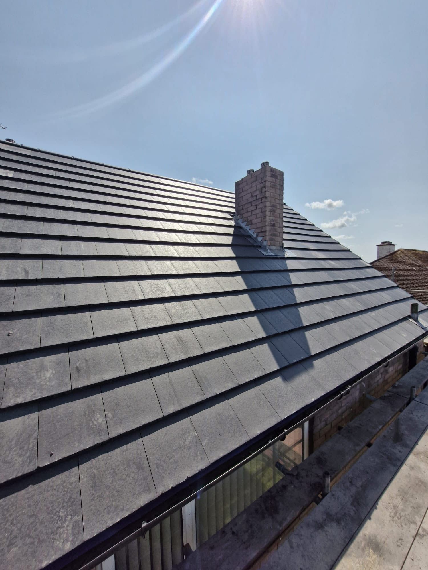 Newly tiled pitched roof with brick chimney and lead flashing in sunshine