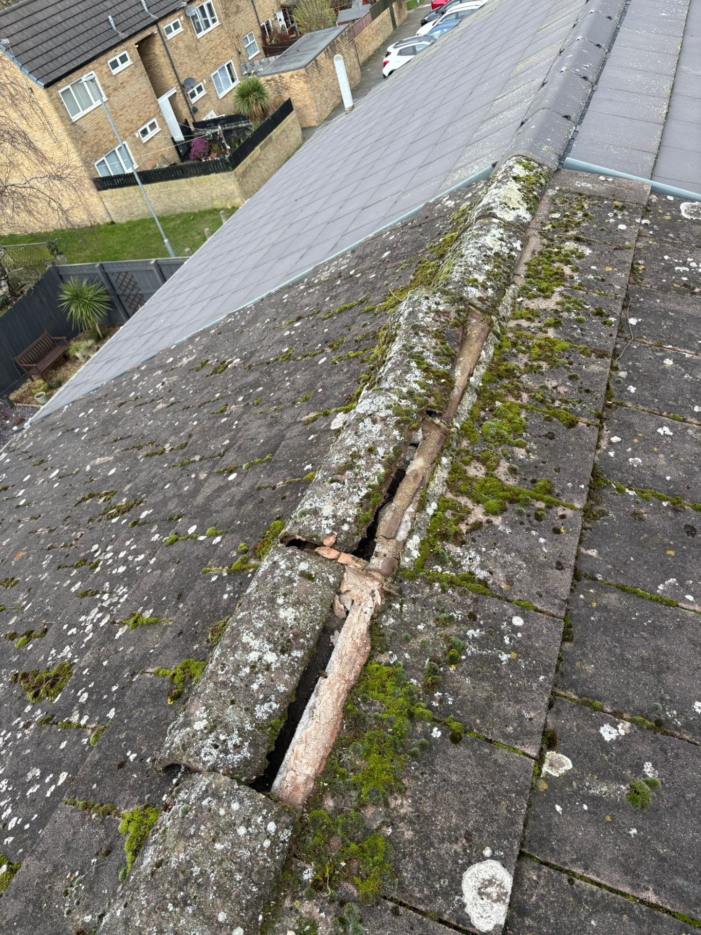 Moss-covered pitched roof with damaged ridge tiles before repair